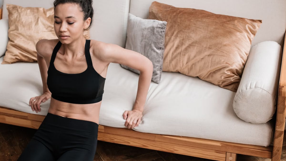 Adult woman in sportswear doing a workout at home on a couch. Focus on fitness and healthy lifestyle.